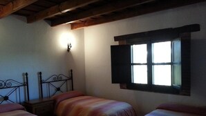 Una habitación con dos camas, una mesita de noche, una lámpara de pared y una ventana con contraventanas.