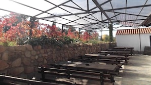 Un área de estar al aire libre con muros de piedra y bancos de madera bajo un techo de metal.