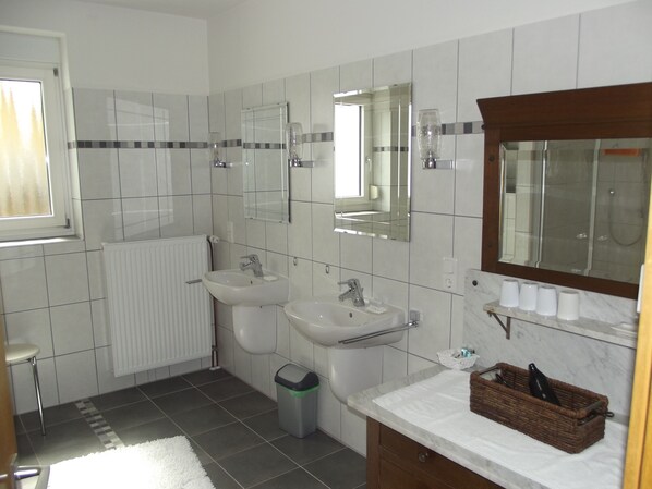 A bathroom with two sinks, a mirror, a radiator, and a trash bin. - Weingut & Gästehaus Kaufmann-Schneider (Erden)