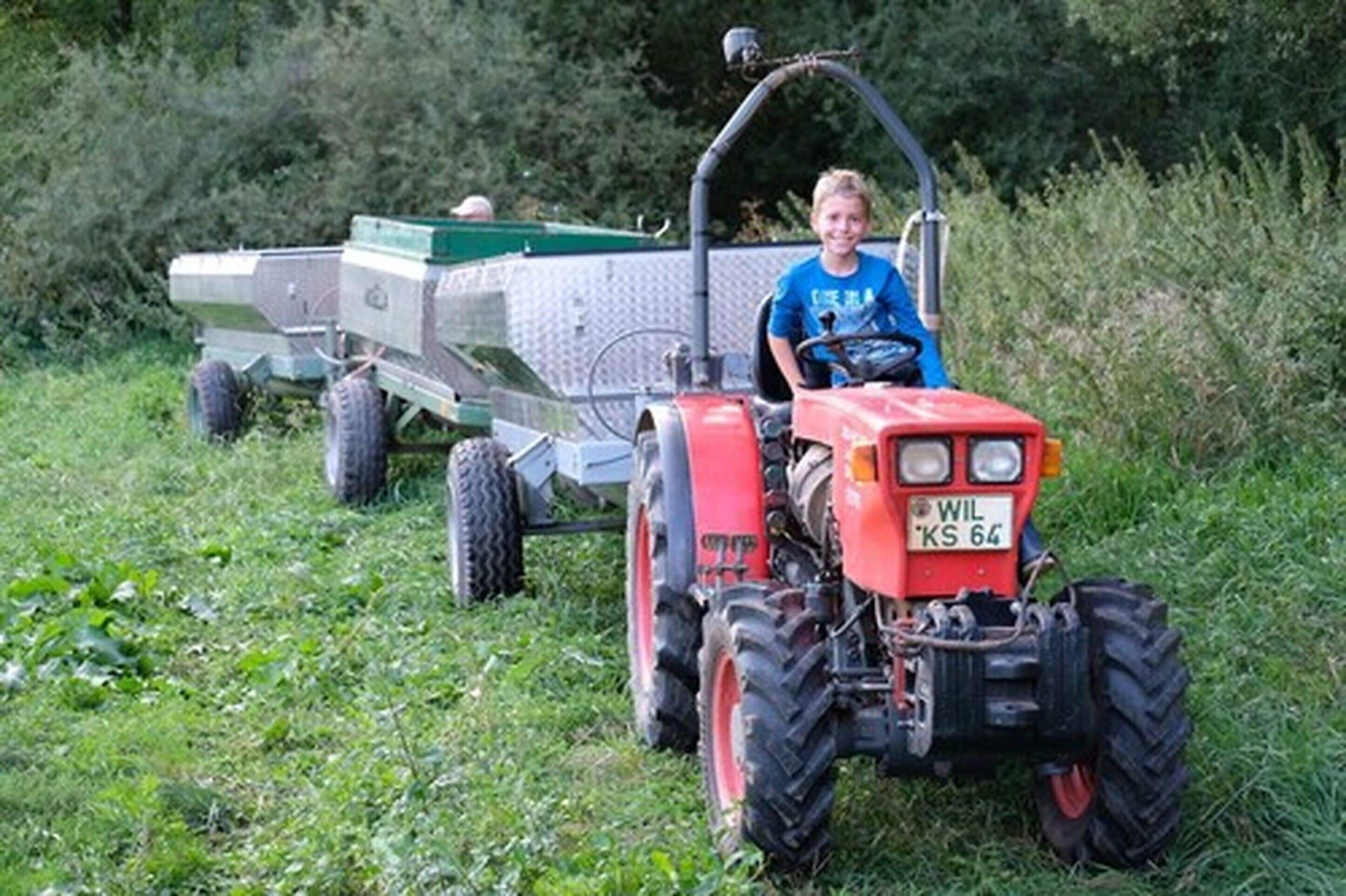 Una persona conduce un tractor rojo con un remolque verde en un campo cubierto de hierba.