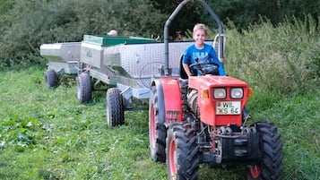Una persona conduce un tractor rojo con un remolque verde en un campo cubierto de hierba.