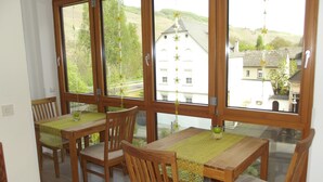A dining area with wooden tables and chairs, large windows with a view of buildings and greenery. - Weingut & Gästehaus Kaufmann-Schneider (Erden)