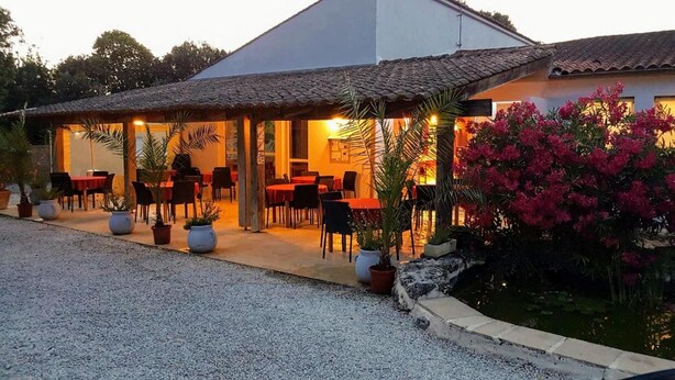 Un edificio con un patio cubierto, mobiliario exterior y plantas en macetas.