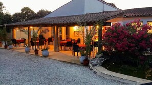 A building with a covered patio area, outdoor seating, and potted plants. - Les Chênes Verts (Saint-Savinien)