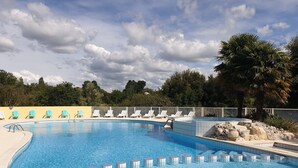 Una piscina con suelo de baldosas, sillones de descanso y una palmera.