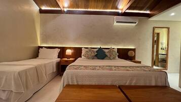 Quarto com duas camas de solteiro, um banco de madeira, mesa de cabeceira com abajur e teto com vigas de madeira e iluminação embutida.
