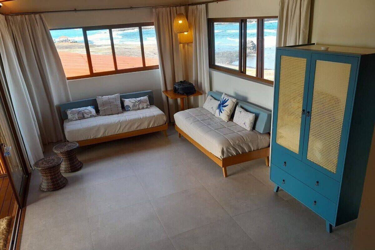 A room with two beds, a blue cabinet, and a view of the beach.