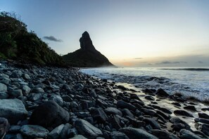 Una playa rocosa con una formación rocosa destacada en la distancia.