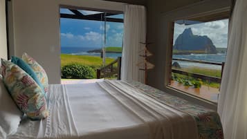 Quarto com cama, vista para o oceano e varanda com grade de madeira.