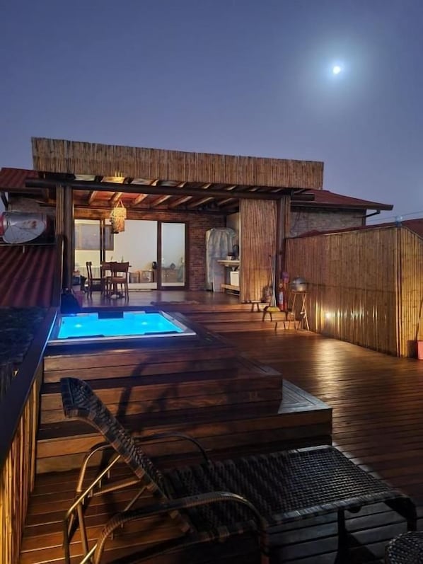 Um deck externo com piscina, móveis de madeira e uma área de estar coberta.