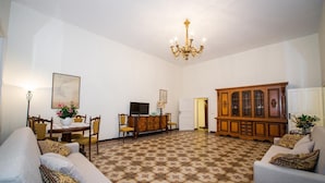 A living room with a patterned carpet, a chandelier, a wooden cabinet, and a television.
