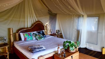 A spacious tented room with a large bed, wooden headboard, and a wooden nightstand with a lamp.