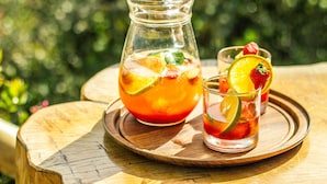 Une carafe et un verre de boisson glacée, avec des tranches de fruits, sur un plateau en bois.