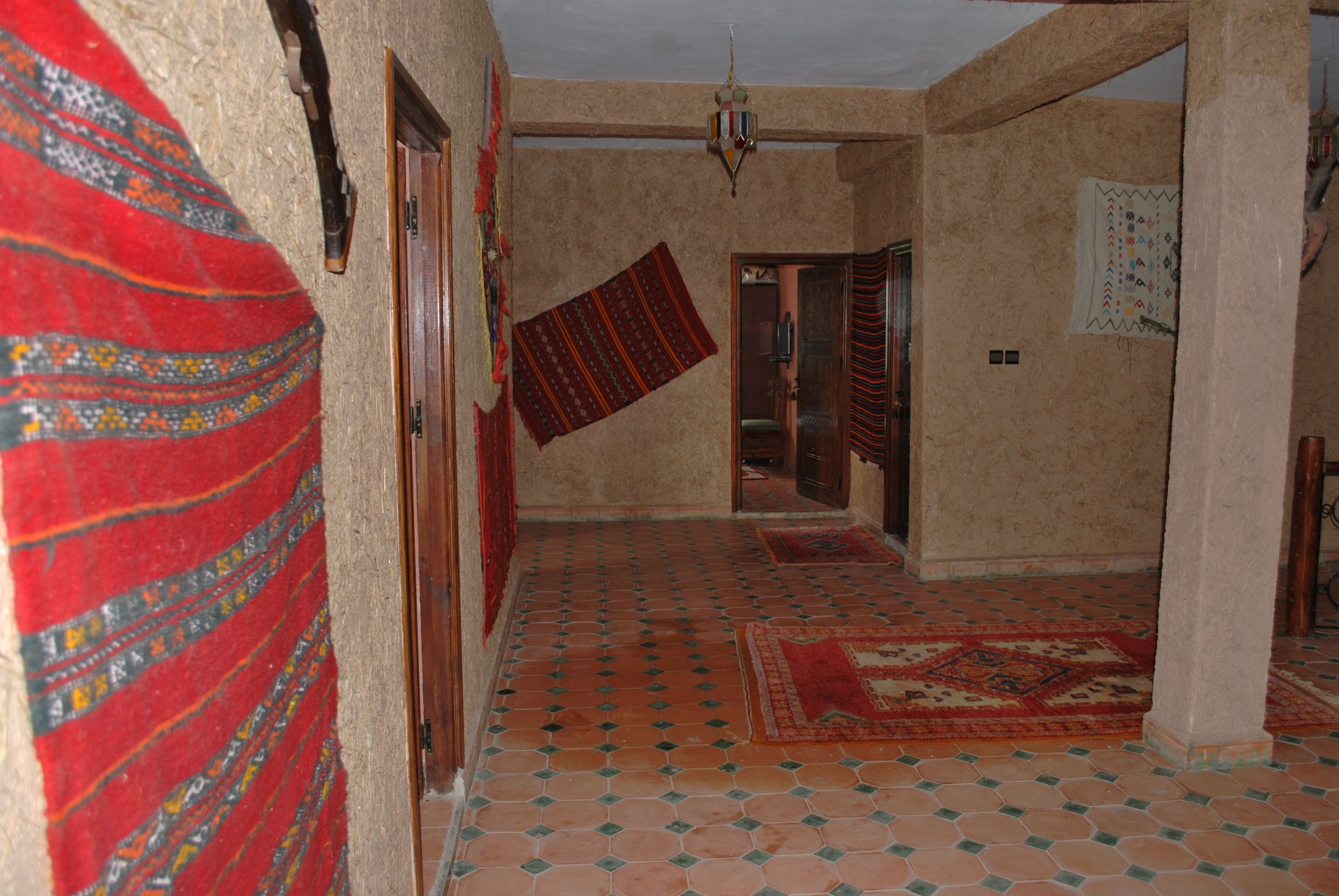 A hallway with patterned rugs, a tiled floor, and a hanging tapestry.