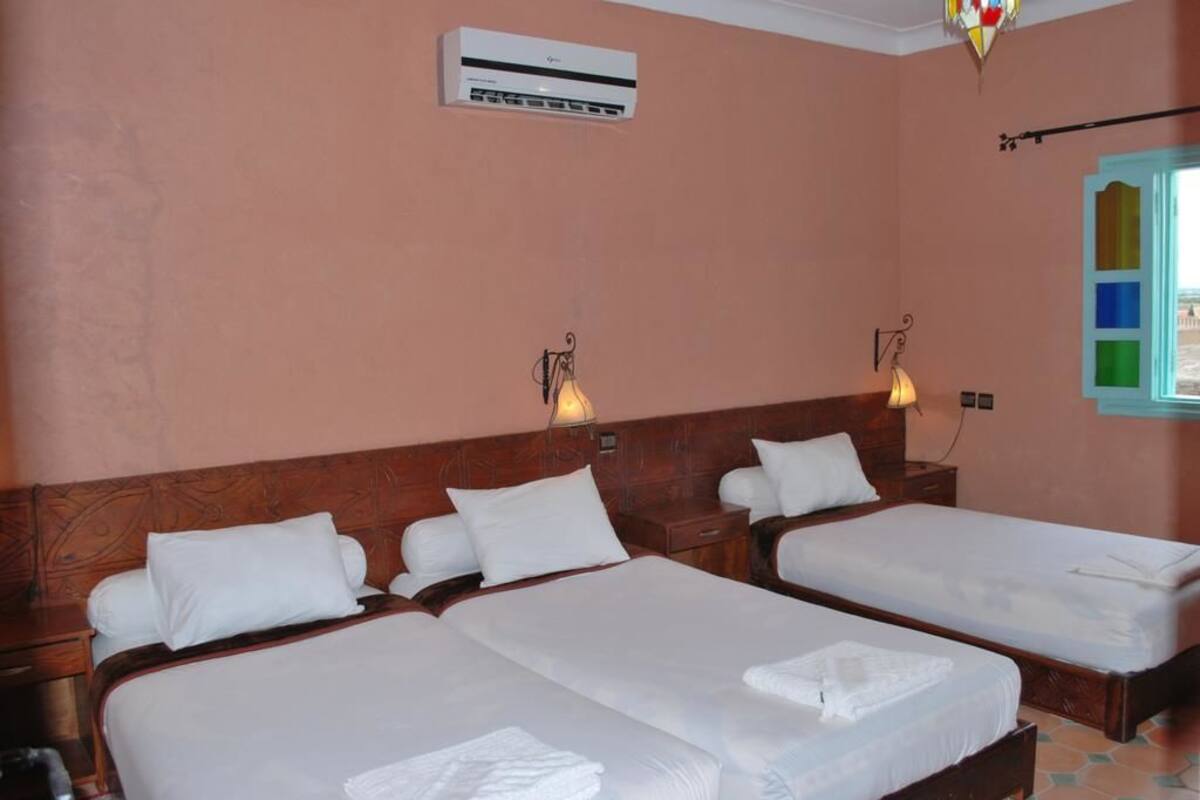 A hotel room with two beds, a wooden headboard, an air conditioning unit, and a window with a colorful view.