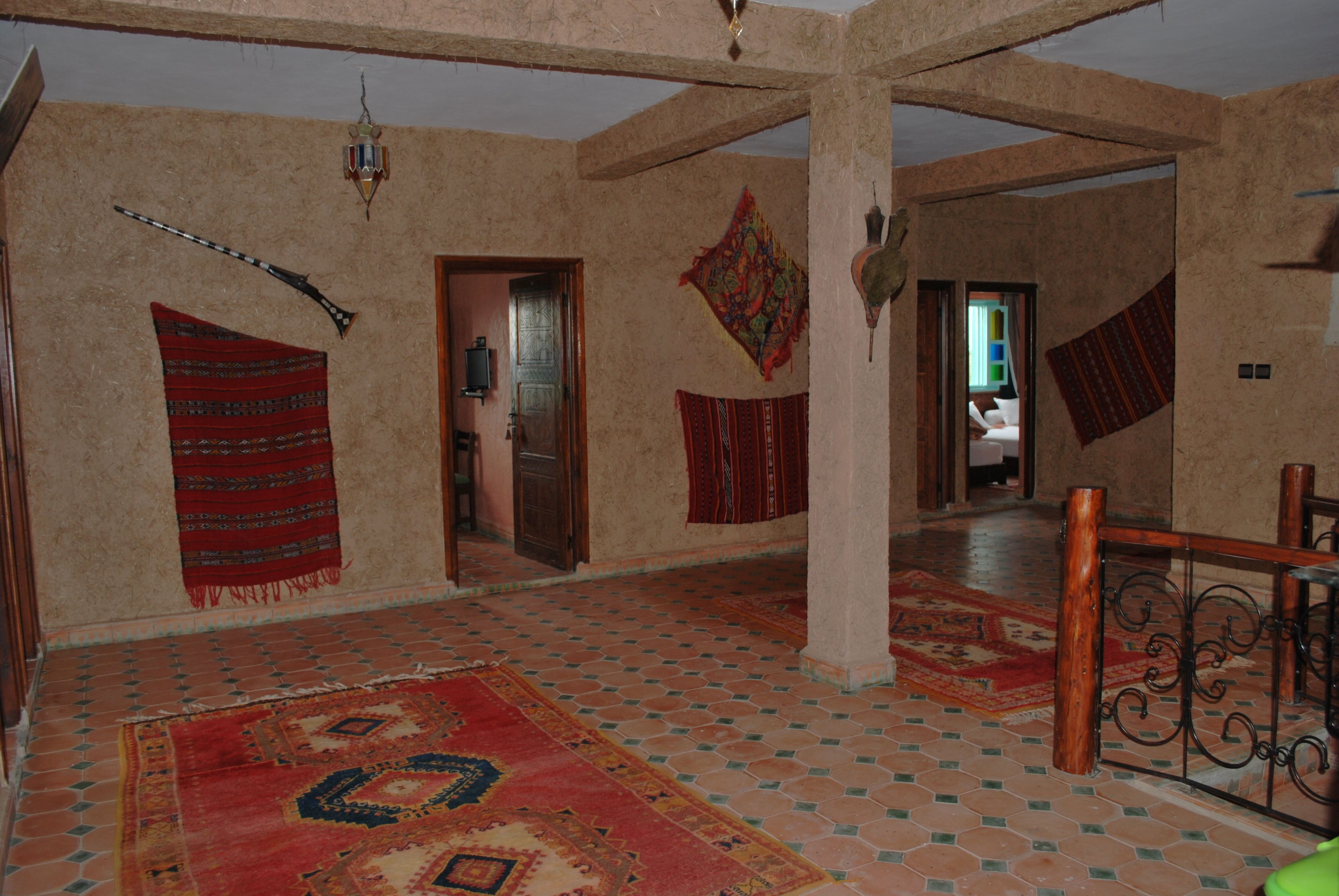 Una habitación amplia con techo alto, vigas de madera a la vista y piso de baldosas. Varias puertas dan acceso a otras áreas, y las paredes están decoradas con textiles estampados.