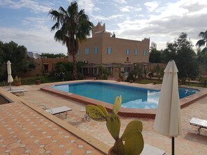 A swimming pool with a hexagonal tiled deck, surrounded by potted plants and umbrellas. - Gite Souss (Issen)