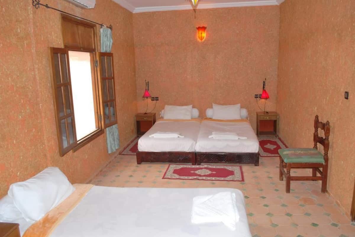 A room with two beds, a window, a wall-mounted lamp, and a chair.