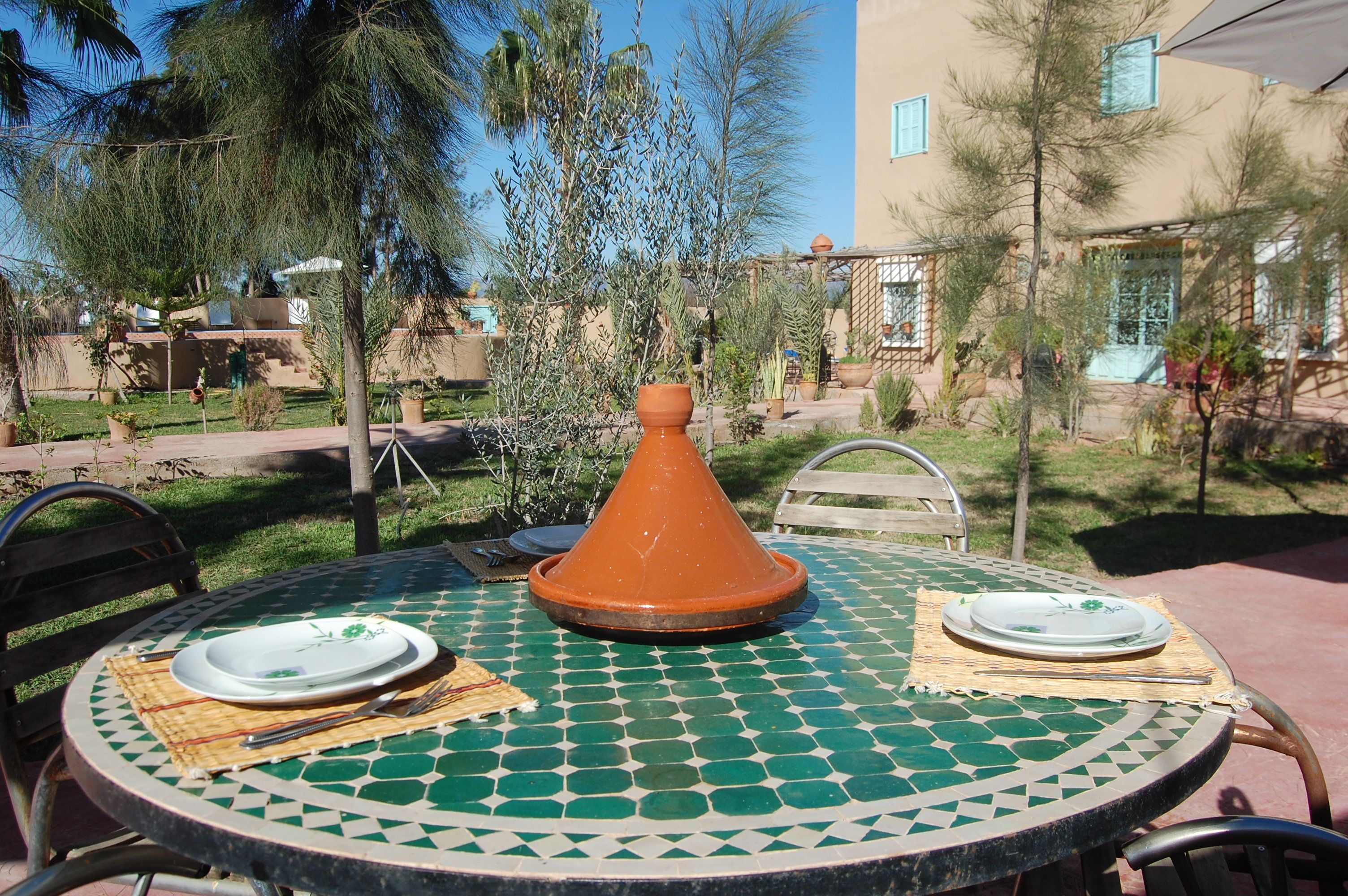 Una mesa redonda con una superficie de mosaico verde y blanco, dos platos blancos con diseños verdes, una servilleta de madera y un tenedor de metal.