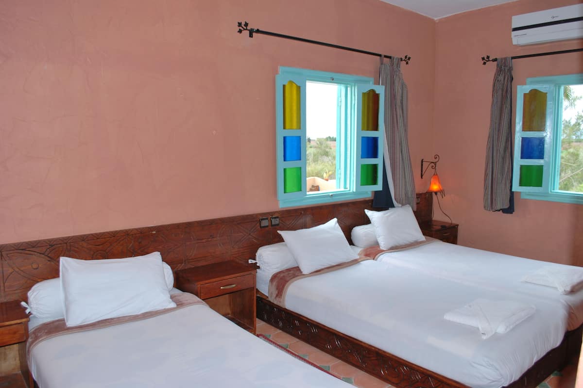 A hotel room with two beds, wooden headboards, a nightstand, and a wall-mounted lamp.
