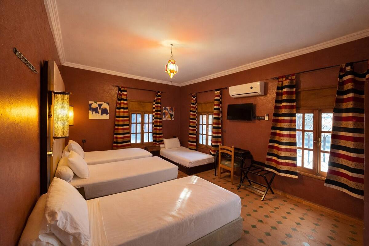 A hotel room with two single beds, a desk, a chair, a television, and a window with striped curtains.