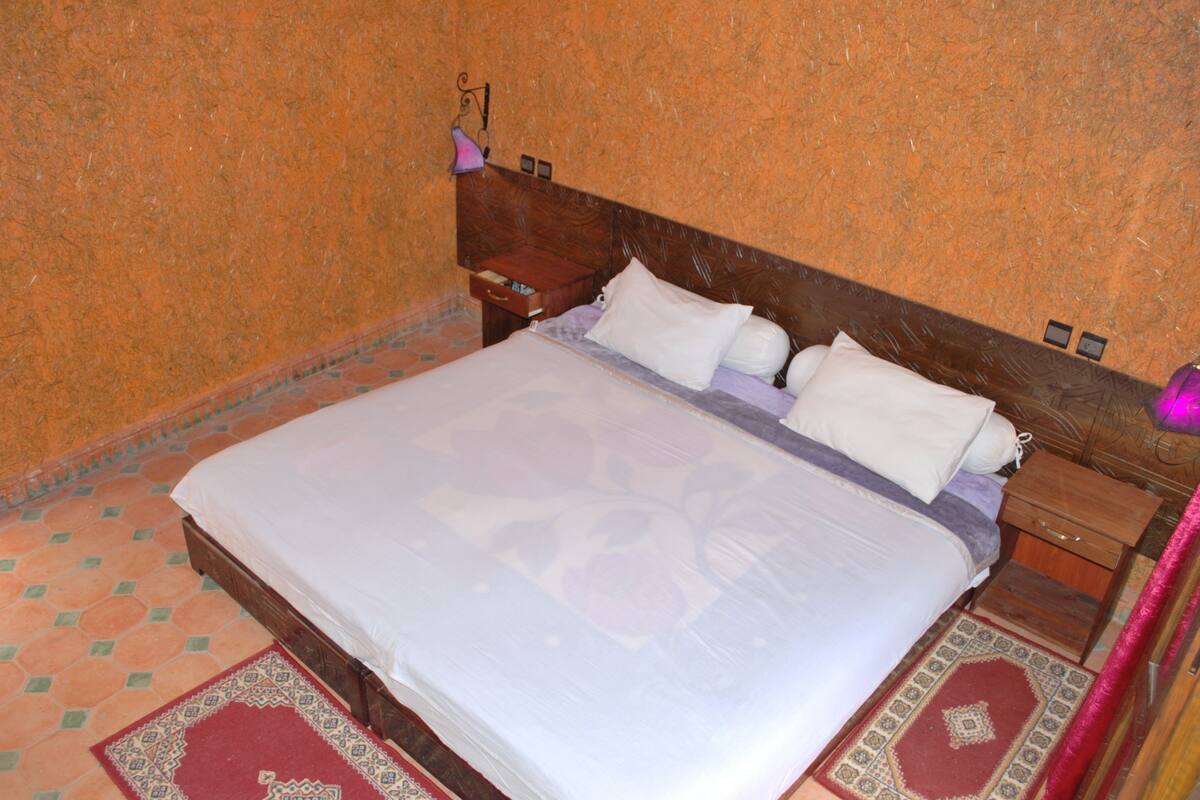 A bedroom with a large bed, wooden headboard, and a nightstand with a lamp.