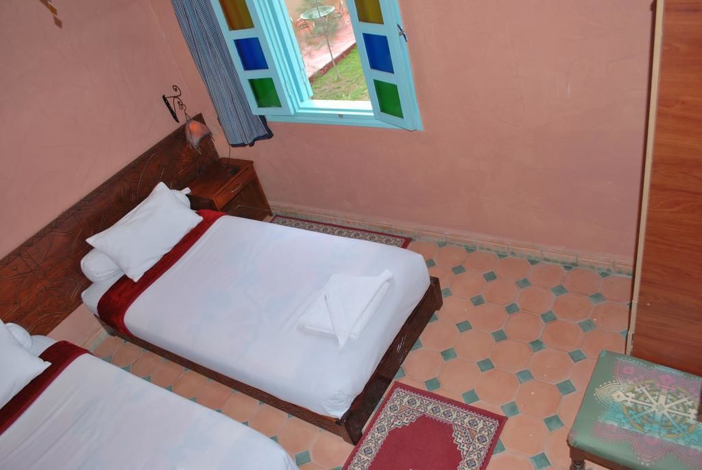A room with two beds, a window with colorful panes, a patterned rug, and a small table.