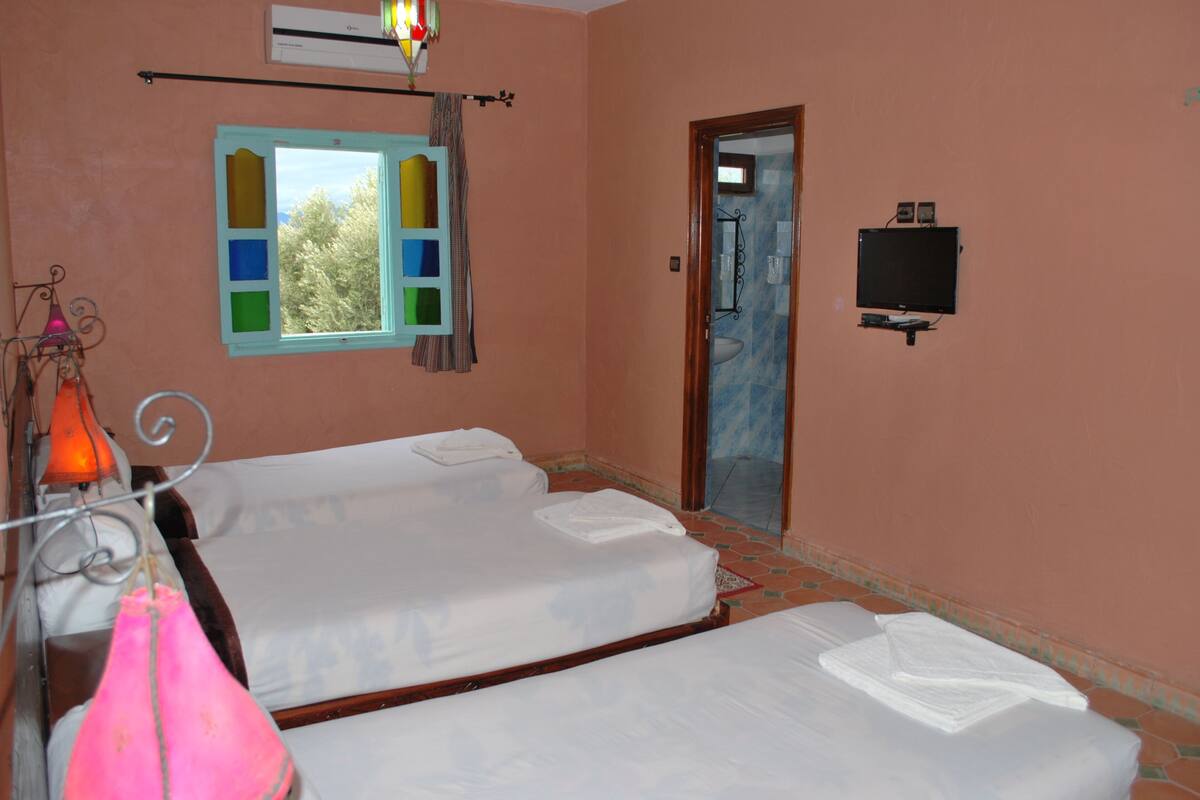 A room with two beds, a window with colorful panes, a mirror, and a television on the wall.