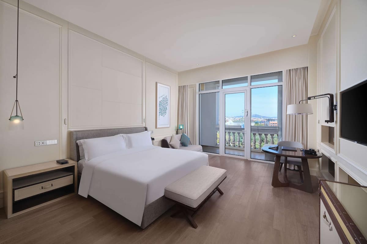 Een hotelkamer met een groot bed, een bureau met stoel, een televisie en een balkon met uitzicht.