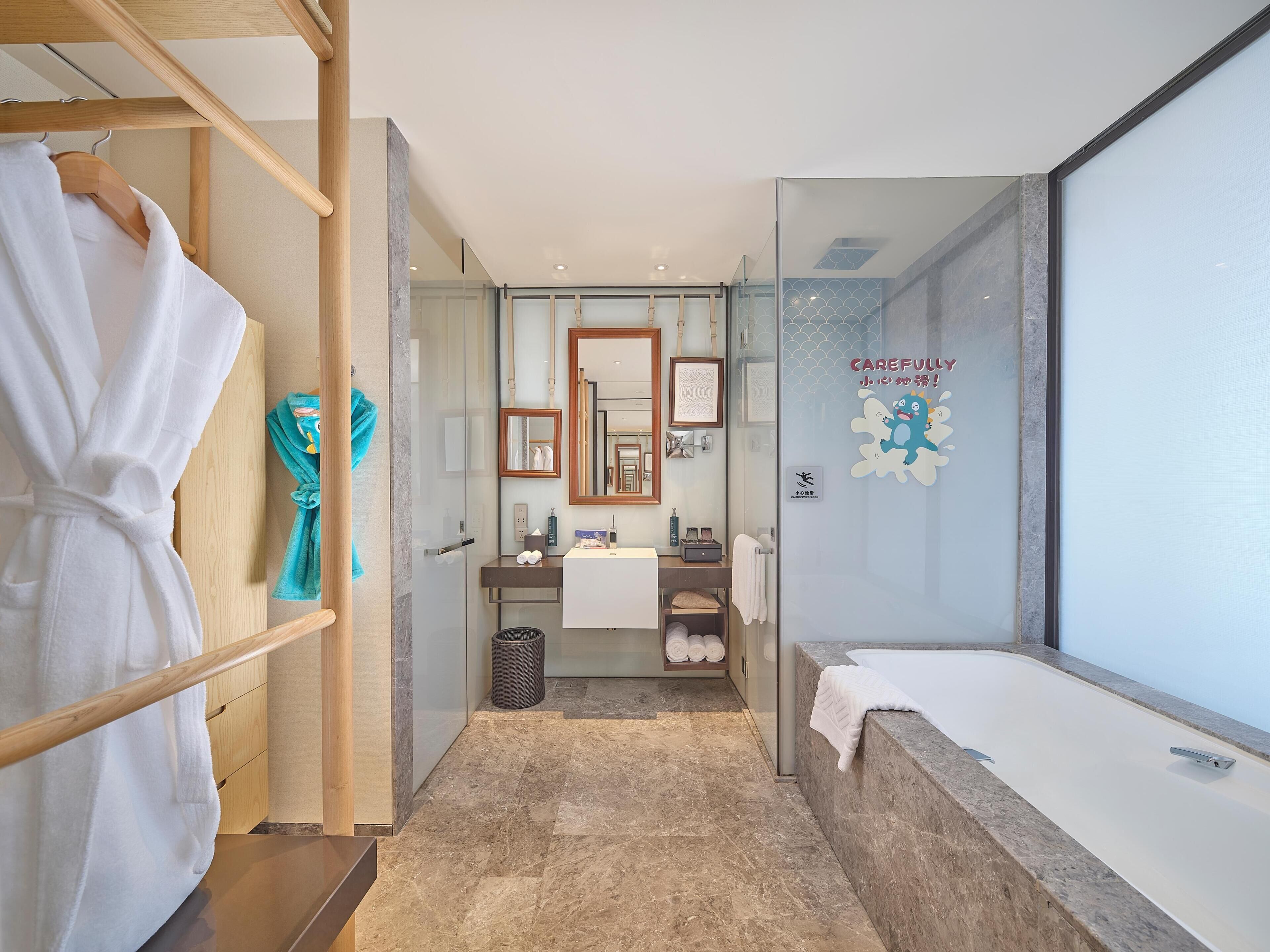 A modern bathroom with a glass shower enclosure, a white bathtub, a vanity with a mirror, and a wooden rack holding a white robe.