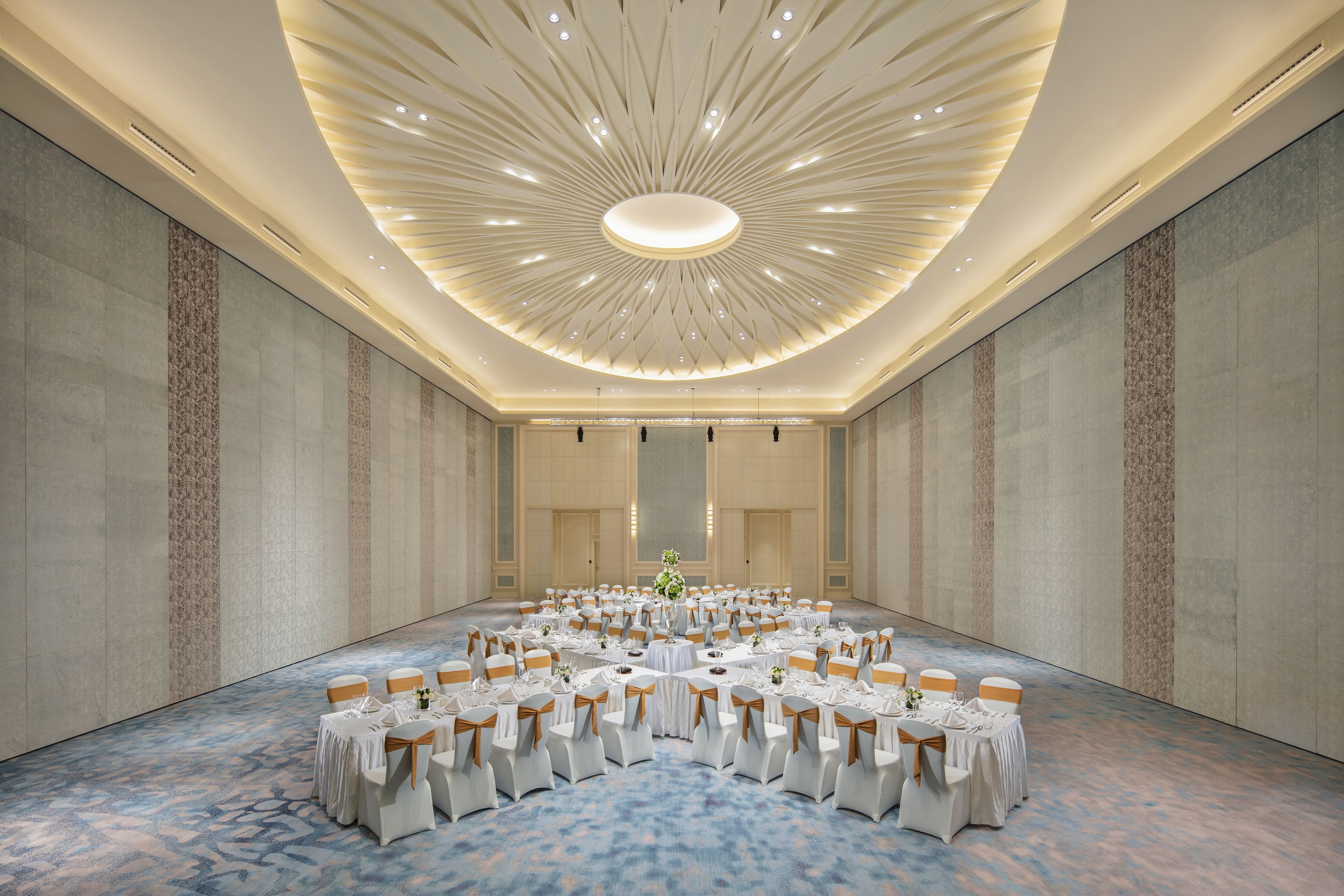 A large conference room with a central table surrounded by chairs, a patterned carpet, and a modern ceiling design.