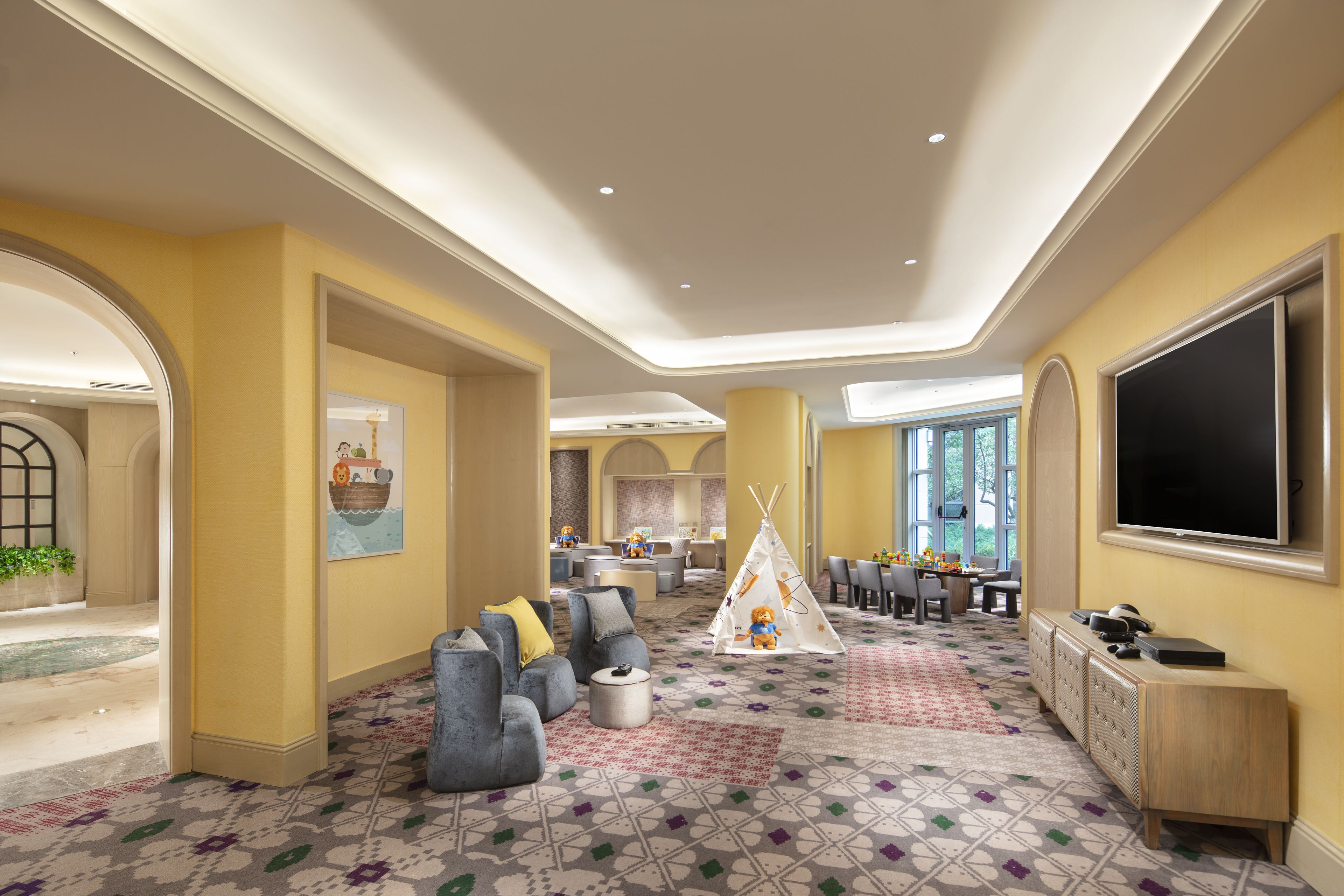 Un amplio vestíbulo de hotel con una gran zona de estar, un área de juegos para niños y un televisor en la pared.