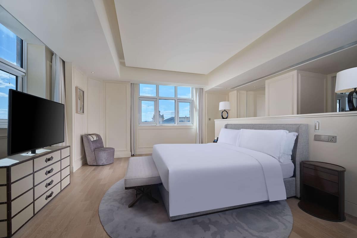 Een moderne hotelkamer met een groot bed, een flatscreen televisie, een bureau met lades, een stoel, een raam met uitzicht en een spiegel.