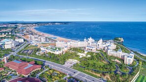 An aerial view of a coastal hotel with multiple buildings, a beachfront, and a well-maintained road network. - Hilton Dalian Golden Pebble Beach Resort (Dalian)