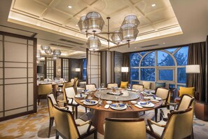 A dining room with a round table set for a meal, surrounded by chairs, and a large window with a view of trees. - Hilton Dalian Golden Pebble Beach Resort (Dalian)
