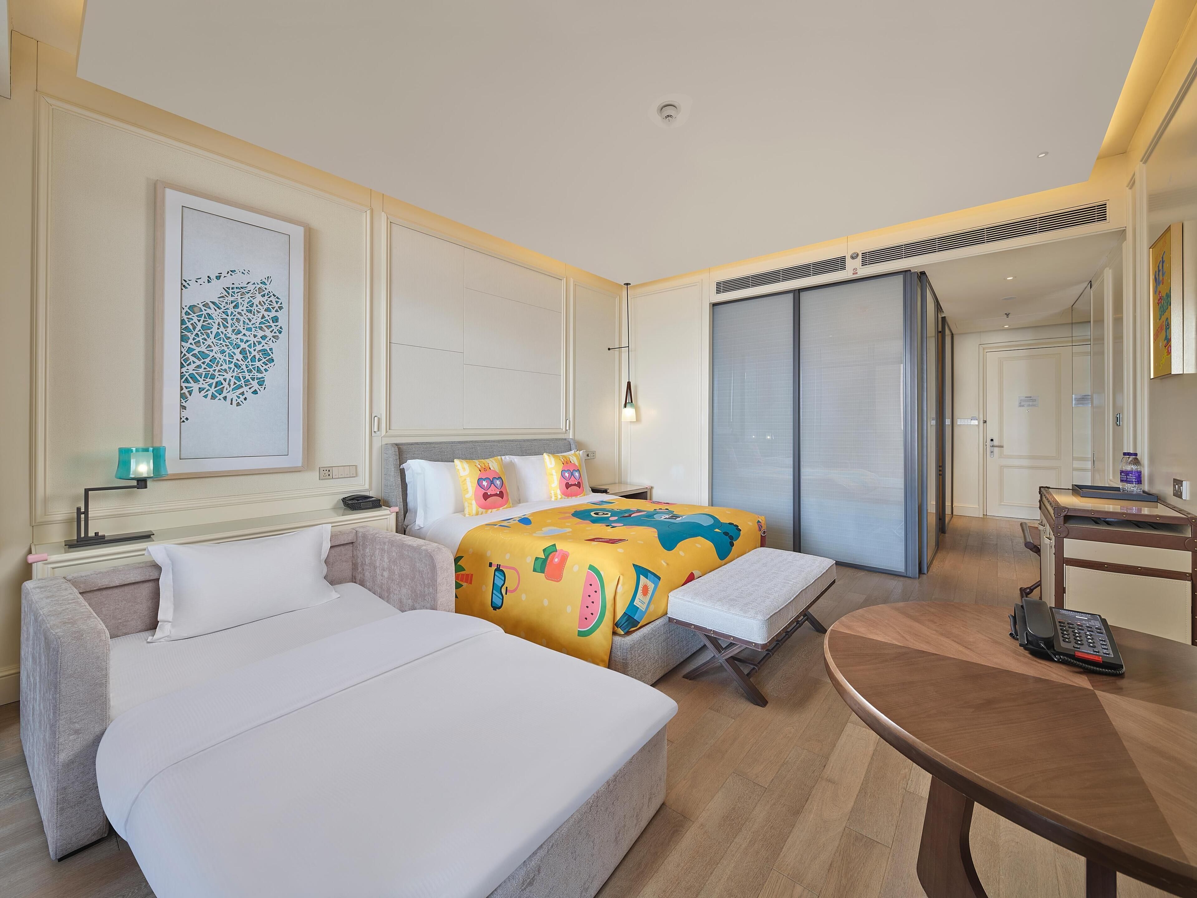 Una habitación de hotel con cama, sofá, escritorio y teléfono, y un ventanal grande.