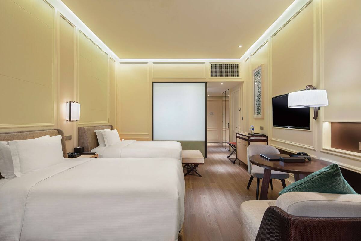 Een hotelkamer met twee bedden, een bureau, een stoel, een televisie en een kleine tafel.