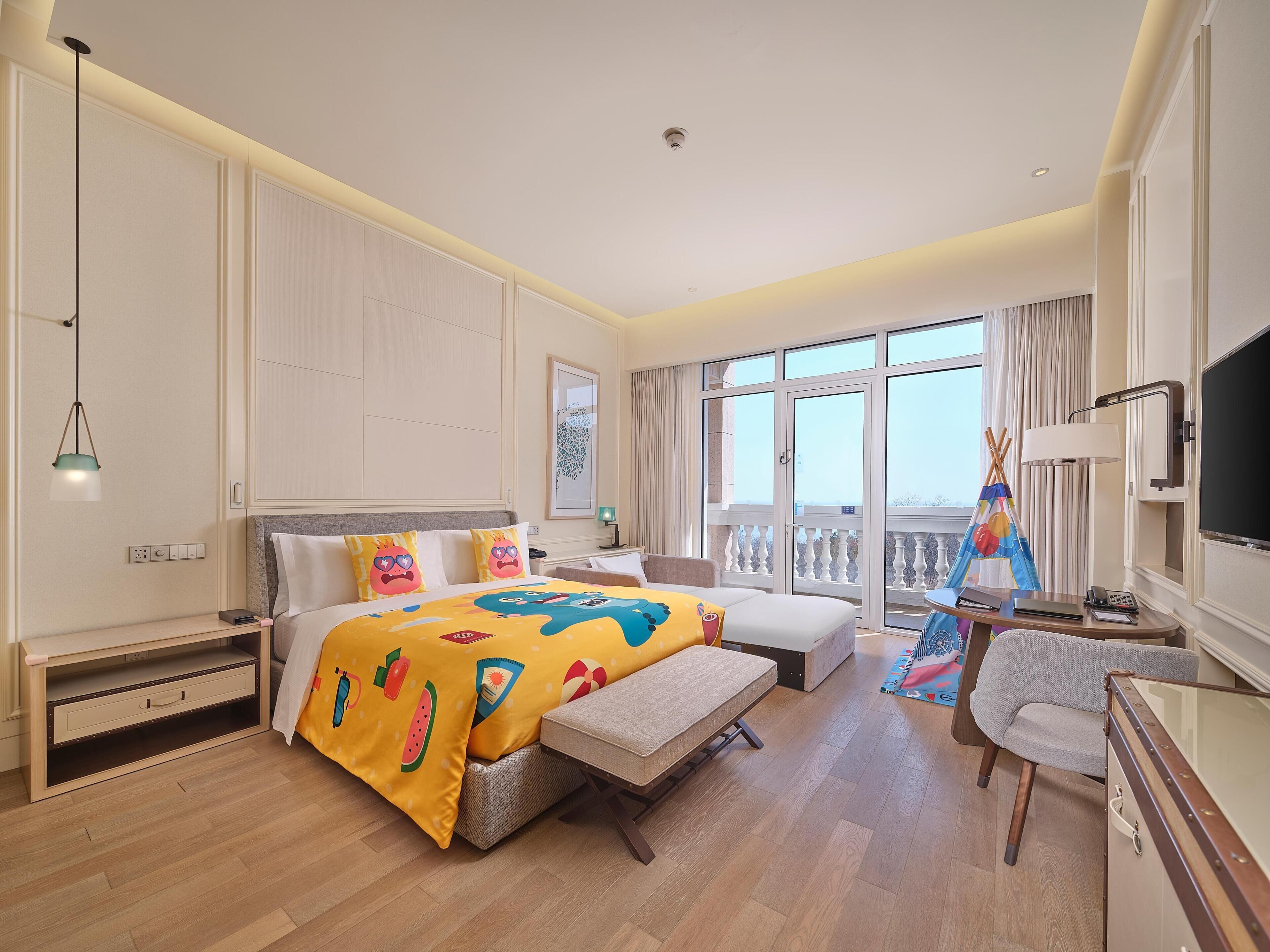 Ein Hotelzimmer mit Bett, Schreibtisch, Stuhl, einem Balkon mit Blick und einem Fernseher.