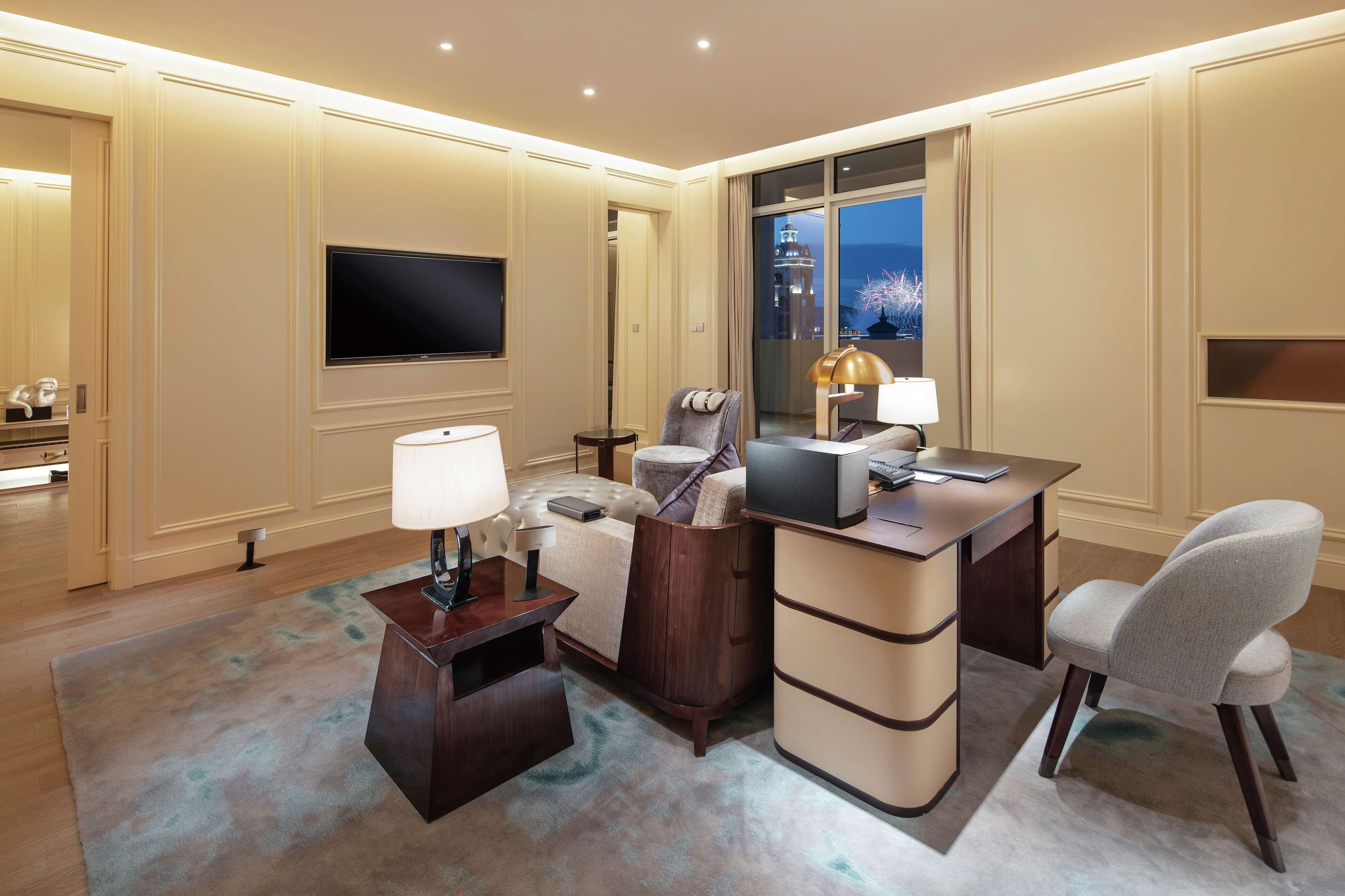 Une chambre d’hôtel moderne équipée d’une télévision à écran plat, d’un bureau avec un ordinateur portable, d’un canapé confortable et d’une grande fenêtre donnant sur la ville.