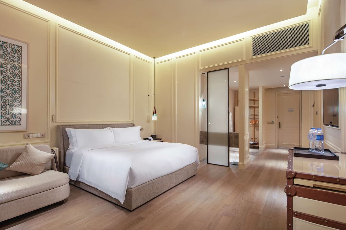 Een hotelkamer met een bed, nachtkastje, lamp en een bureau met stoel.