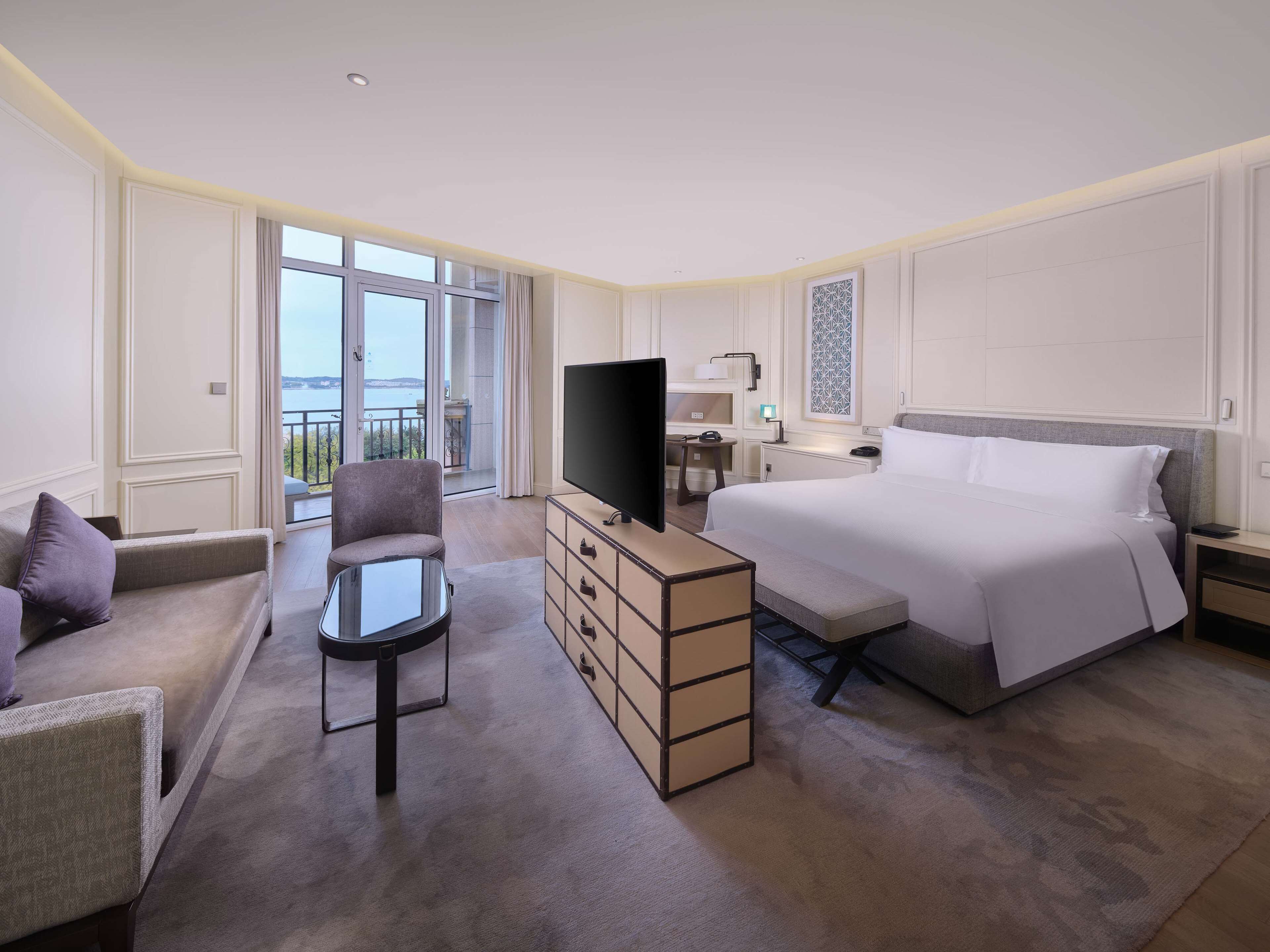 Habitación de hotel con una cama grande, un escritorio con televisor, una silla y vista al mar.