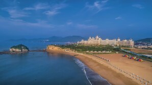 Un hôtel situé sur la côte, doté d’un grand bâtiment, d’une plage et donnant sur l’océan.