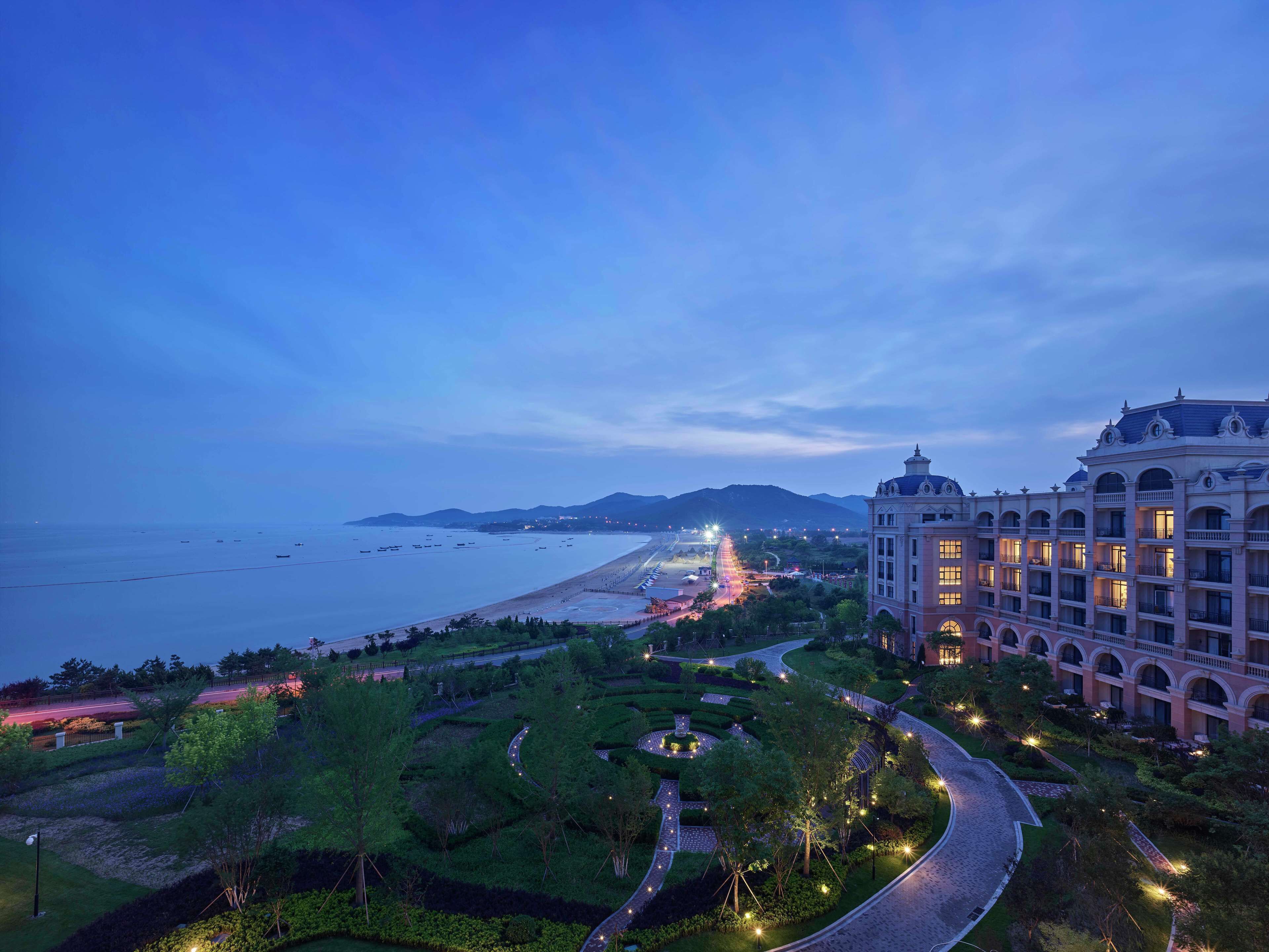 Un hotel frente al mar con jardín ajardinado, vistas a la playa y un camino bien iluminado.