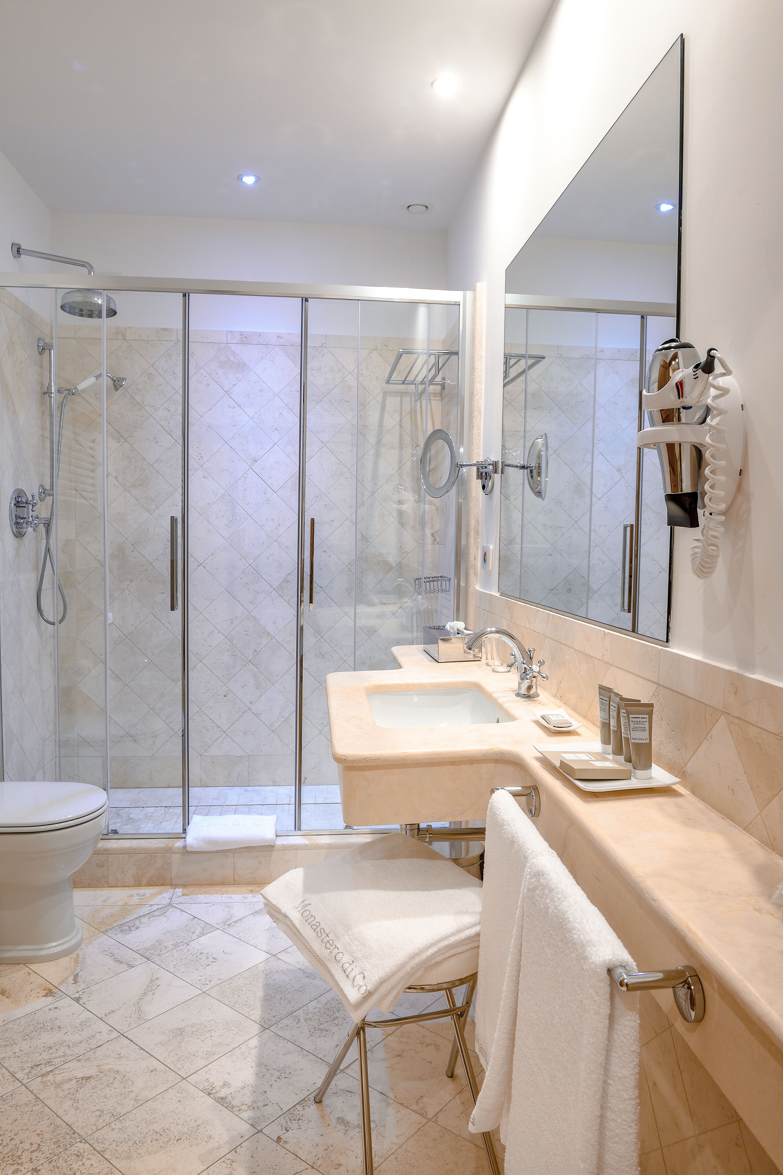 Un baño moderno con ducha de vidrio, un espejo grande, un lavamanos con artículos de aseo y un inodoro.