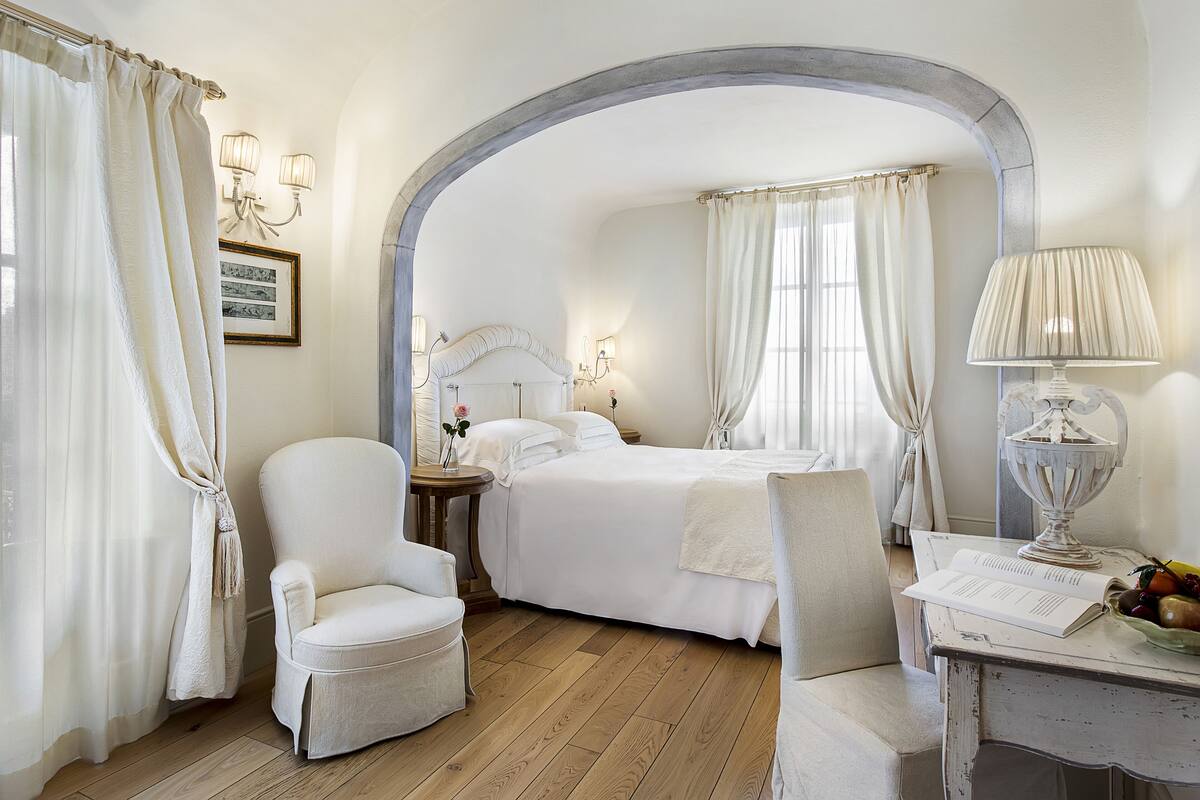 Een hotelkamer met een bed, twee stoelen, een tafel met een lamp en een schaal fruit.