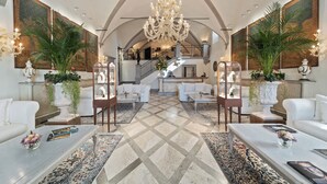 Eine geräumige Lobby mit hoher Decke, einem prunkvollen Kronleuchter und einer Treppe zu einer oberen Ebene.