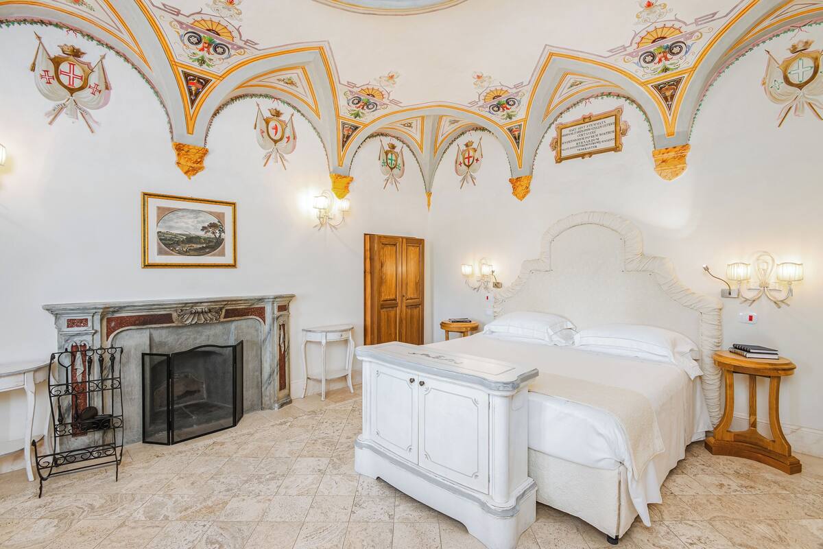 Een luxueuze slaapkamer met een groot bed, een open haard en gedetailleerde plafonddecoraties.
