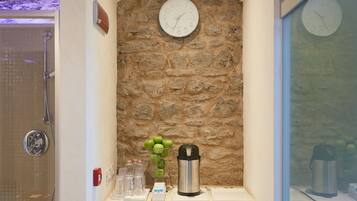 Une salle de bain avec un mur en pierre, une horloge, une douche et un plan de travail sur lequel se trouvent une bouilloire et des bouteilles.