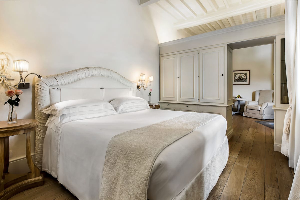 Een groot bed met hoofdeinde, bedlampen en een vaas met bloemen.