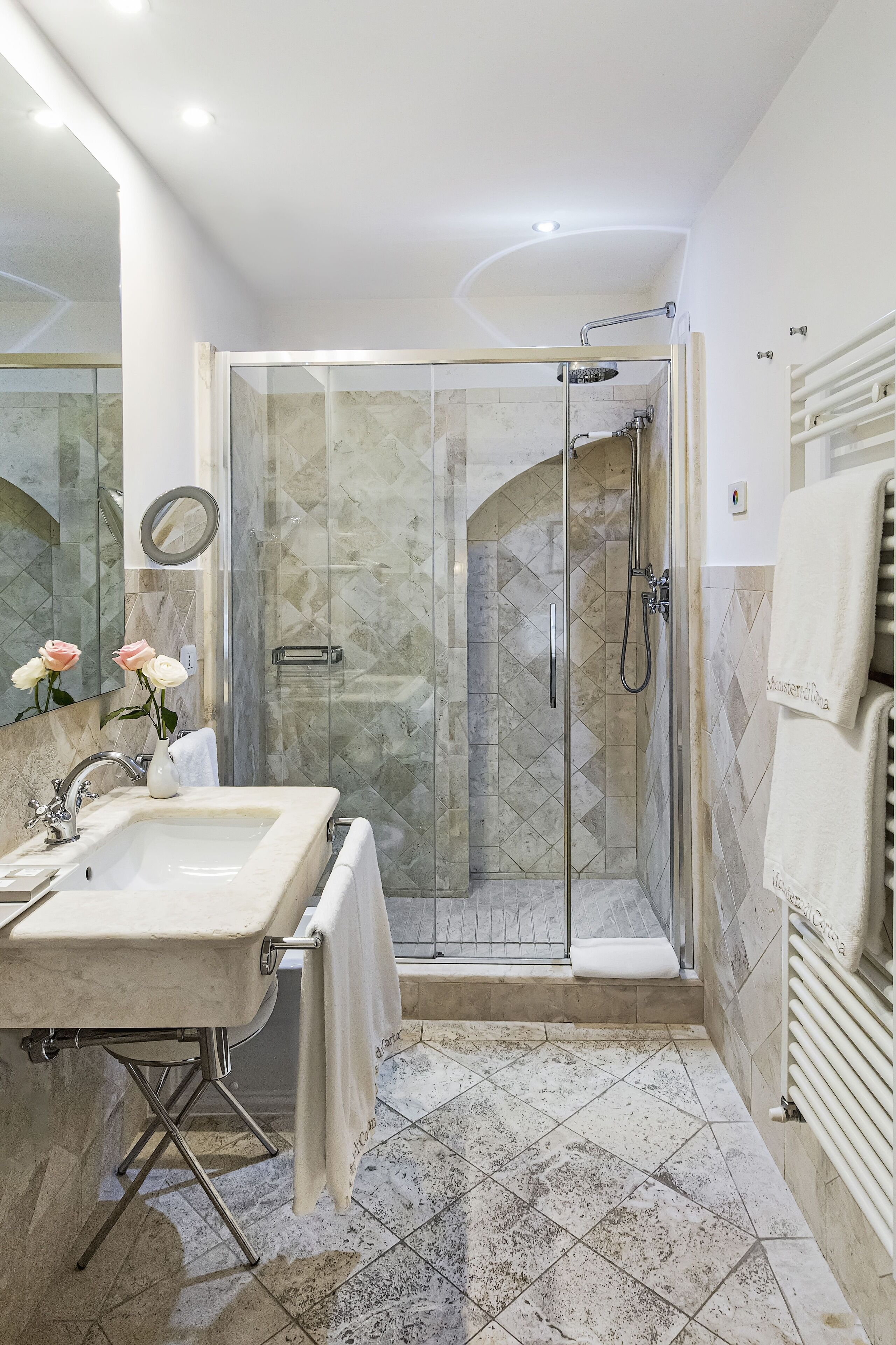 A modern bathroom with a glass-enclosed shower, a marble sink, and a tiled floor.
